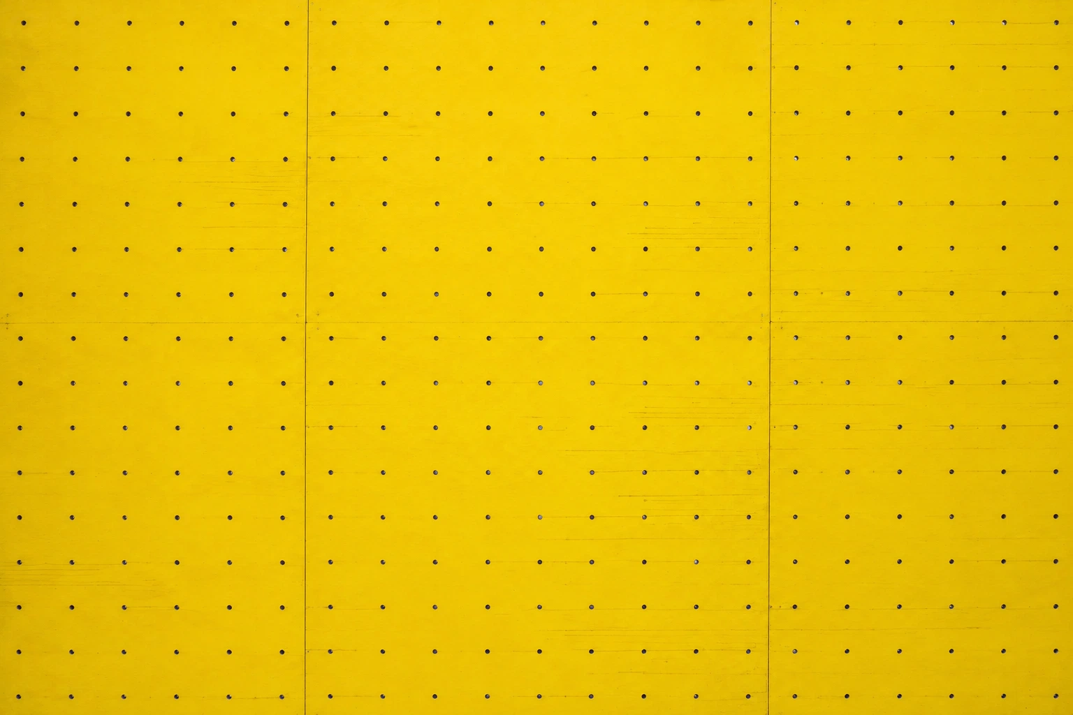 A wide, straight-on view of a single yellow plywood climbing wall with rows of empty mounting holes.